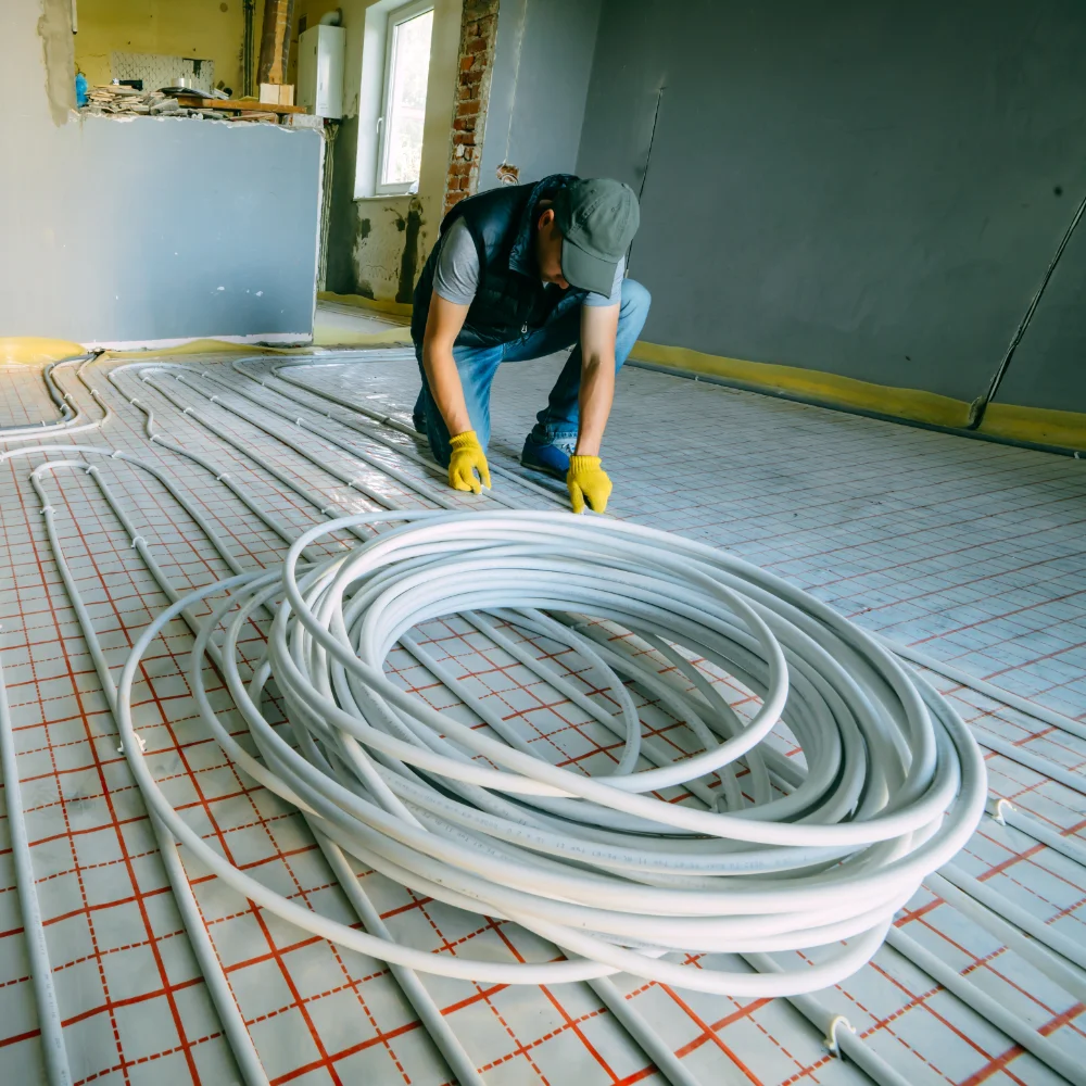Installer laying underfloor heating pipework across insulation panels in a room