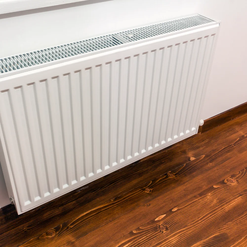 White panel radiator installed on an interior wall above a wooden floor.